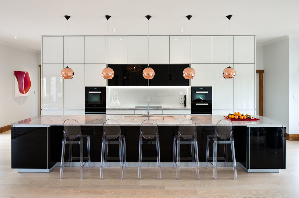 Moderne Küche mit flächenbündigen Schrankfronten, Küchenrückwand in Weiß, schwarzen Elektrogeräten und Kücheninsel in Wellington