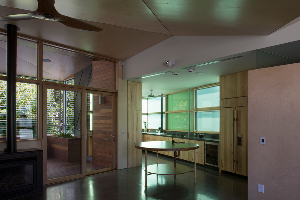 Стильный дизайн: кухня в современном стиле с светлыми деревянными фасадами, зеленым фартуком, бетонным полом и островом - последний тренд