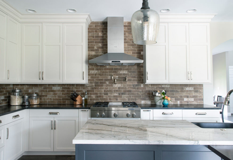 Photo of a l-shaped kitchen in Other with a belfast sink, white cabinets, engineered stone countertops, beige splashback, ceramic splashback, stainless steel appliances, an island and grey floors.