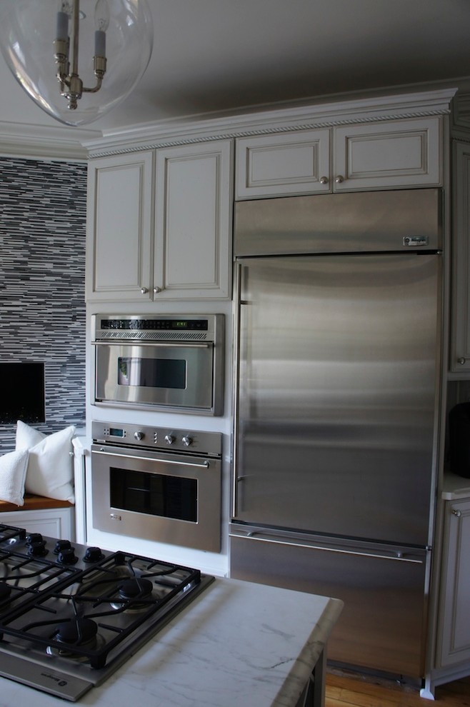 Idéer för ett avskilt, litet klassiskt u-kök, med en undermonterad diskho, luckor med upphöjd panel, vita skåp, marmorbänkskiva, vitt stänkskydd, stänkskydd i mosaik, rostfria vitvaror, ljust trägolv och en köksö