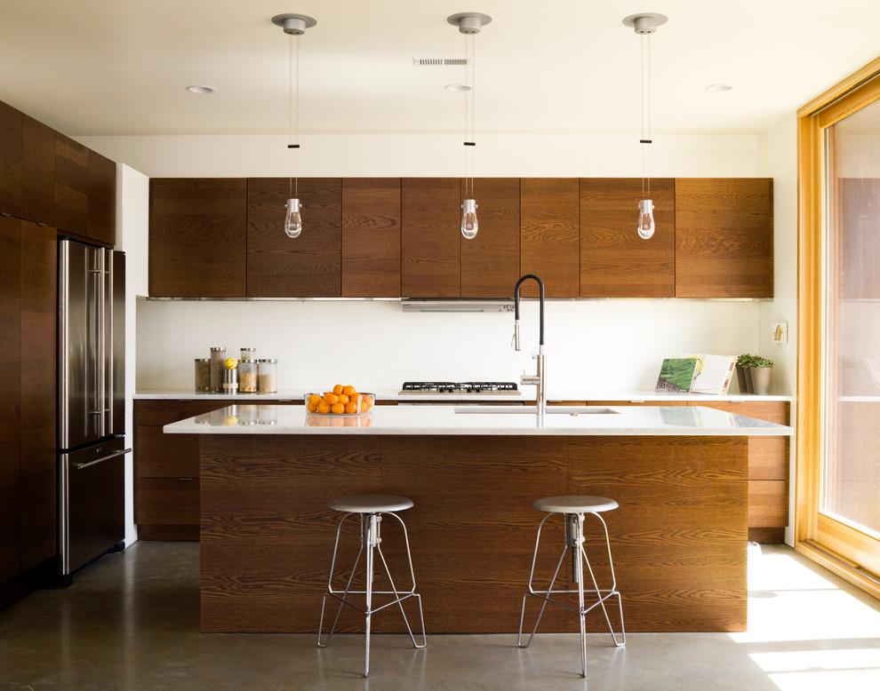 Immagine di una cucina moderna con lavello sottopiano, ante lisce, ante in legno scuro, elettrodomestici in acciaio inossidabile, paraspruzzi bianco e pavimento in cemento