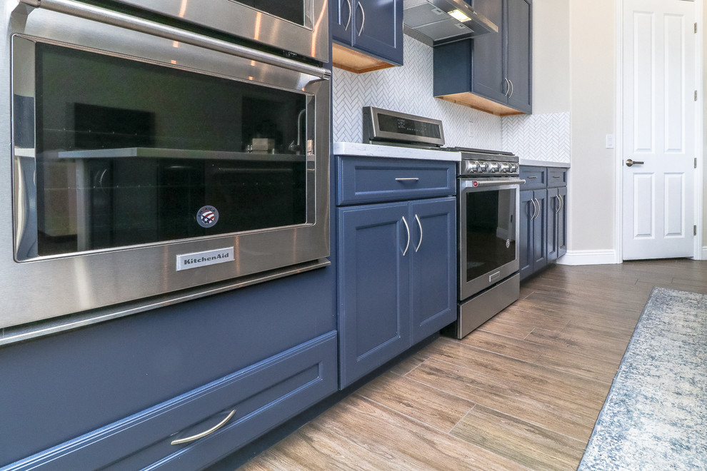 Modern inredning av ett mellanstort vit vitt kök, med en undermonterad diskho, luckor med infälld panel, blå skåp, bänkskiva i kvarts, vitt stänkskydd, rostfria vitvaror, klinkergolv i porslin, en köksö och brunt golv