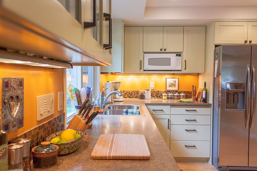 Example of a mid-sized classic u-shaped light wood floor eat-in kitchen design in Other with a drop-in sink, flat-panel cabinets, green cabinets, laminate countertops, multicolored backsplash, glass tile backsplash, stainless steel appliances and a peninsula