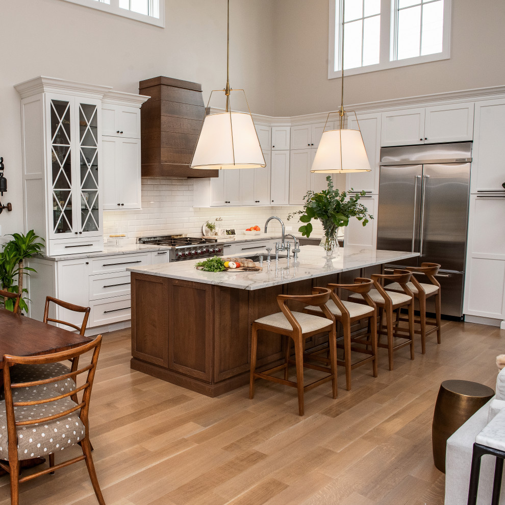 Kitchen - transitional l-shaped medium tone wood floor and brown floor kitchen idea in New York with an undermount sink, shaker cabinets, white cabinets, white backsplash, subway tile backsplash, stainless steel appliances, an island and gray countertops