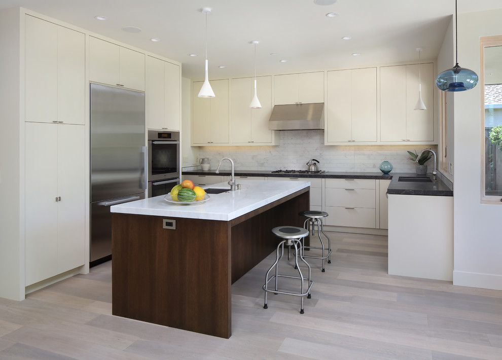 Photo of a contemporary u-shaped kitchen in San Francisco with a submerged sink, flat-panel cabinets, beige cabinets, stainless steel appliances, white splashback and stone tiled splashback.