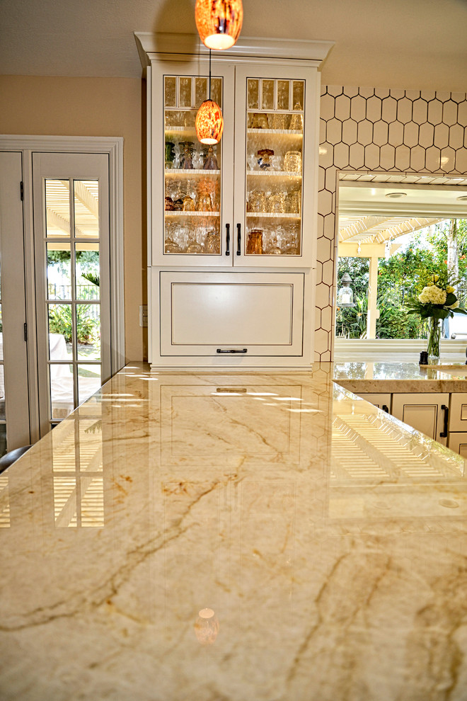 Example of a mid-sized transitional l-shaped travertine floor eat-in kitchen design in San Diego with a farmhouse sink, shaker cabinets, white cabinets, granite countertops, white backsplash, ceramic backsplash, stainless steel appliances and a peninsula
