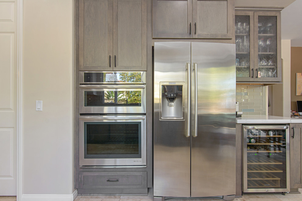 This is an example of a large modern grey and white l-shaped kitchen/diner in San Diego with flat-panel cabinets, grey cabinets, grey splashback, glass tiled splashback, stainless steel appliances, porcelain flooring, beige floors, white worktops, a submerged sink and engineered stone countertops.