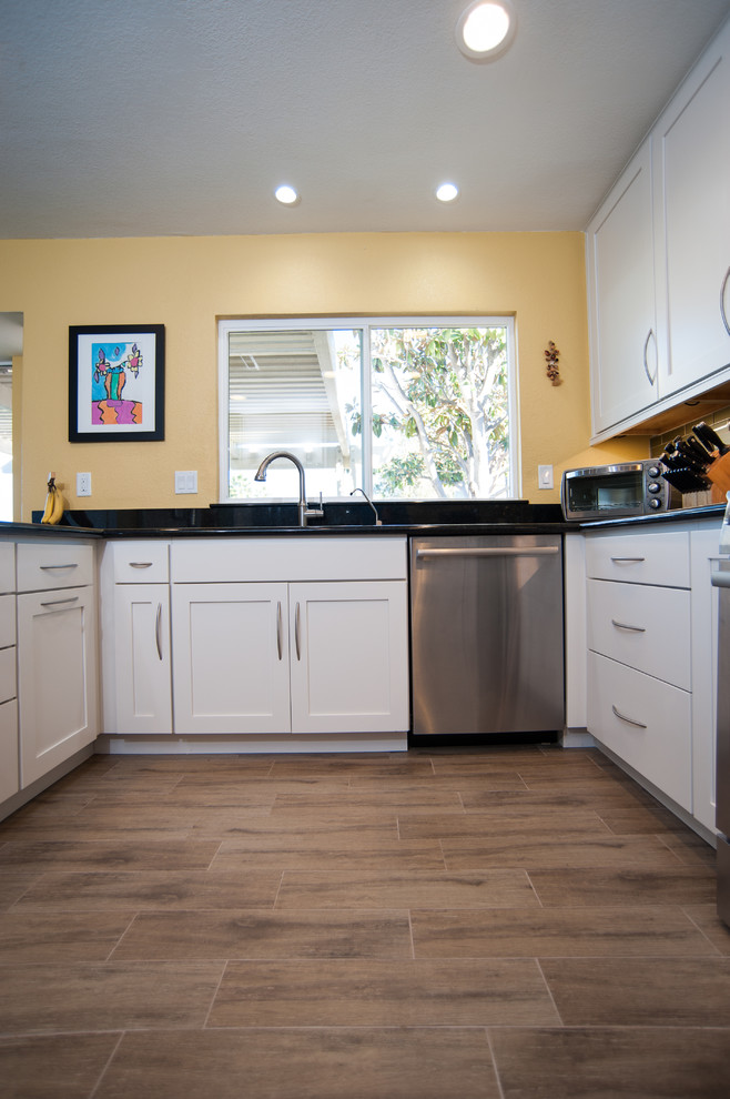 Photo of a medium sized traditional u-shaped enclosed kitchen in San Diego with a built-in sink, recessed-panel cabinets, white cabinets, quartz worktops, green splashback, glass tiled splashback, stainless steel appliances, light hardwood flooring and a breakfast bar.