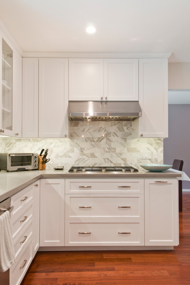 Example of a mid-sized transitional u-shaped light wood floor and brown floor enclosed kitchen design in Los Angeles with an undermount sink, shaker cabinets, white cabinets, quartzite countertops, white backsplash, marble backsplash, stainless steel appliances, a peninsula and gray countertops