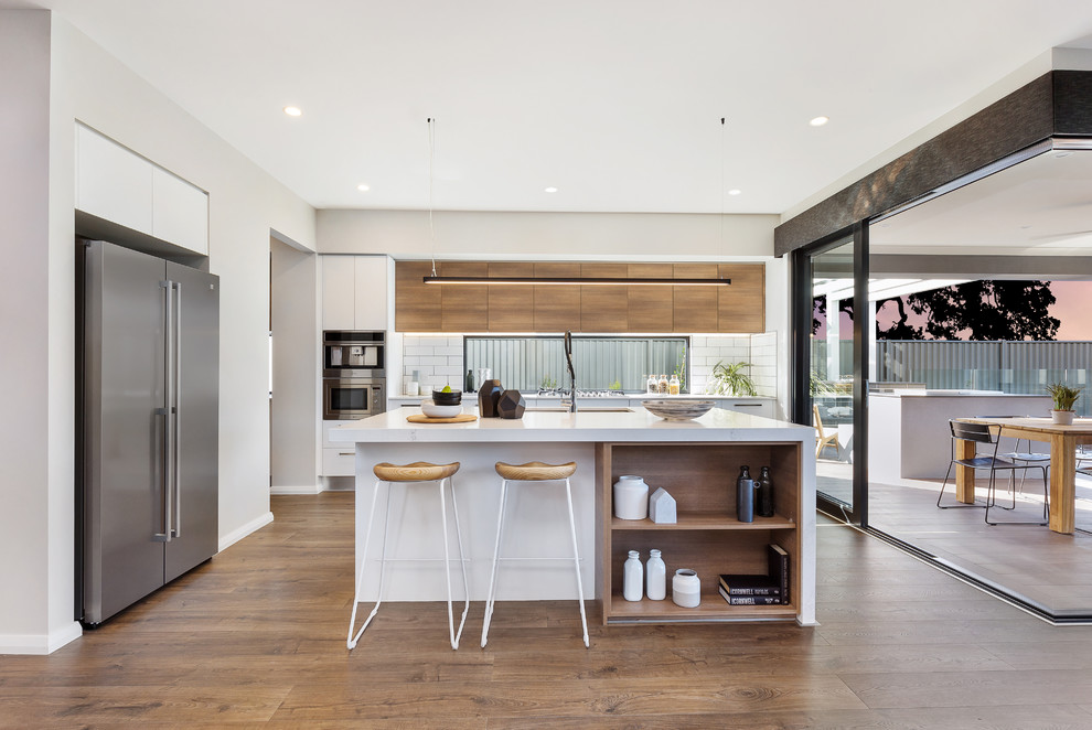 Example of a trendy medium tone wood floor and brown floor kitchen design in Sydney with an undermount sink, flat-panel cabinets, medium tone wood cabinets, white backsplash, subway tile backsplash, stainless steel appliances, an island and white countertops