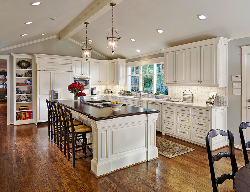 Inspiration for a traditional u-shaped kitchen/diner in Orange County with raised-panel cabinets, white cabinets, grey splashback, stainless steel appliances, an island and dark hardwood flooring.