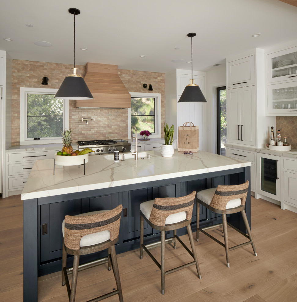Design ideas for a country l-shaped open plan kitchen in San Francisco with a submerged sink, flat-panel cabinets, white cabinets, engineered stone countertops, beige splashback, ceramic splashback, integrated appliances, light hardwood flooring, an island and white worktops.