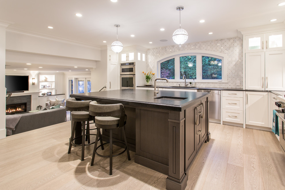 Photo of a large traditional l-shaped kitchen/diner in Vancouver with a submerged sink, shaker cabinets, white cabinets, granite worktops, grey splashback, marble splashback, stainless steel appliances, medium hardwood flooring, an island, beige floors and black worktops.