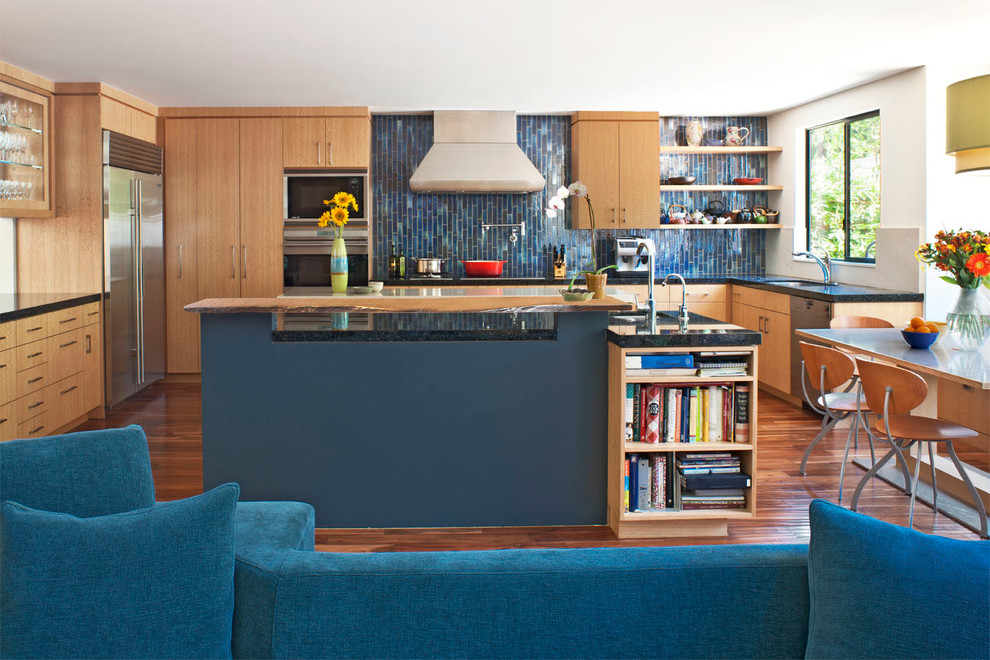 Пример оригинального дизайна: кухня-гостиная в современном стиле с техникой из нержавеющей стали, деревянной столешницей, плоскими фасадами, светлыми деревянными фасадами и синим фартуком