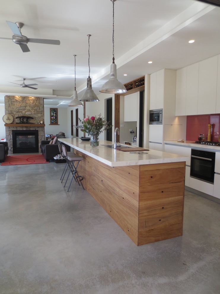 シドニーにあるお手頃価格の中くらいなコンテンポラリースタイルのおしゃれなキッチン (アンダーカウンターシンク、ガラス板のキッチンパネル、黒い調理設備、コンクリートの床、白いキャビネット、赤いキッチンパネル) の写真