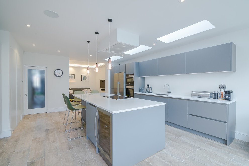 Medium sized contemporary galley kitchen/diner in London with a submerged sink, flat-panel cabinets, grey cabinets, quartz worktops, white splashback, stainless steel appliances, light hardwood flooring, an island, brown floors and white worktops.