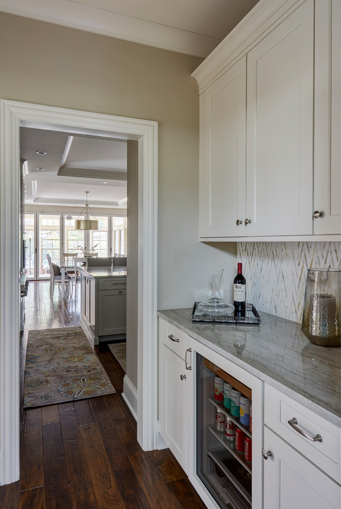 Klassisk inredning av ett mellanstort kök, med en dubbel diskho, luckor med upphöjd panel, vita skåp, marmorbänkskiva, grått stänkskydd, stänkskydd i marmor, rostfria vitvaror, mörkt trägolv och en köksö
