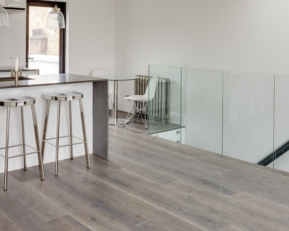 Moderne Küche mit flächenbündigen Schrankfronten, weißen Schränken, Edelstahl-Arbeitsplatte, braunem Holzboden und Kücheninsel in London