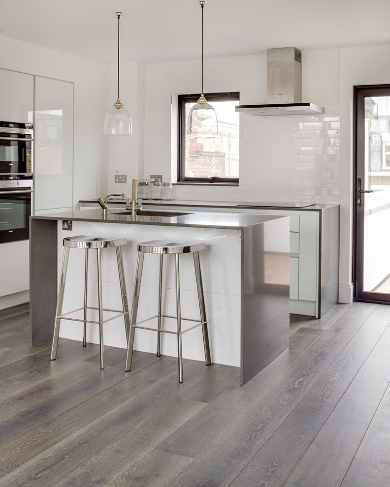 Diseño de cocina contemporánea con armarios con paneles lisos, puertas de armario blancas, encimera de acero inoxidable, suelo de madera en tonos medios y una isla