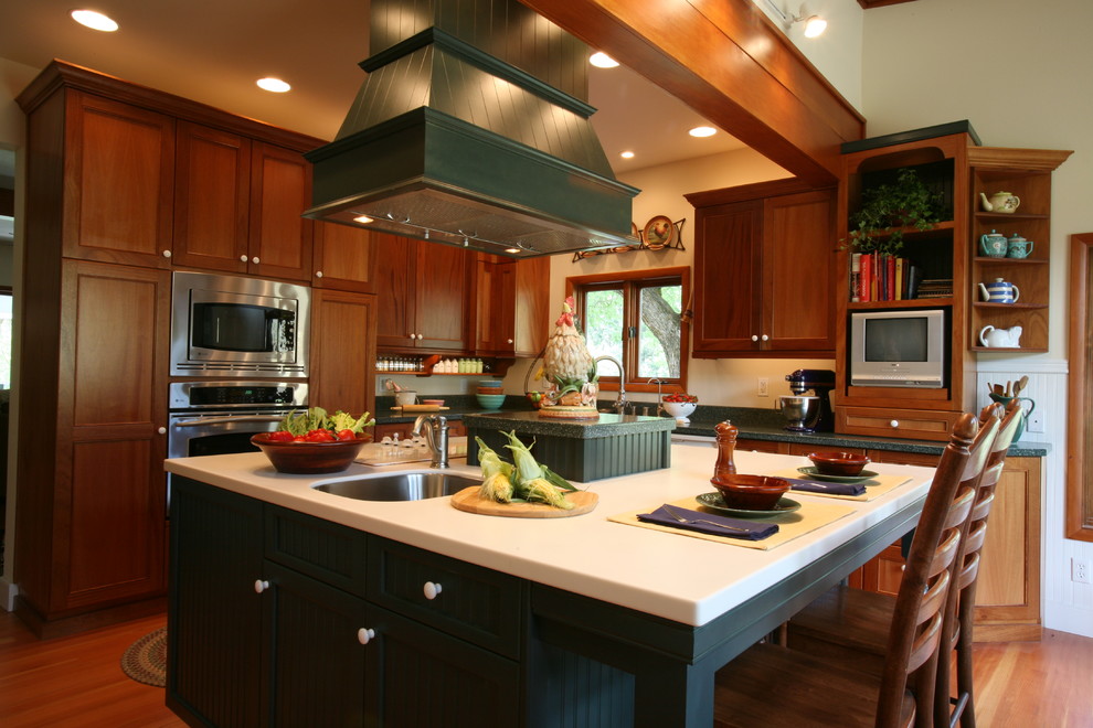 Lantlig inredning av ett kök, med en rustik diskho, luckor med profilerade fronter, gröna skåp, bänkskiva i koppar, grönt stänkskydd, rostfria vitvaror, mellanmörkt trägolv och en köksö