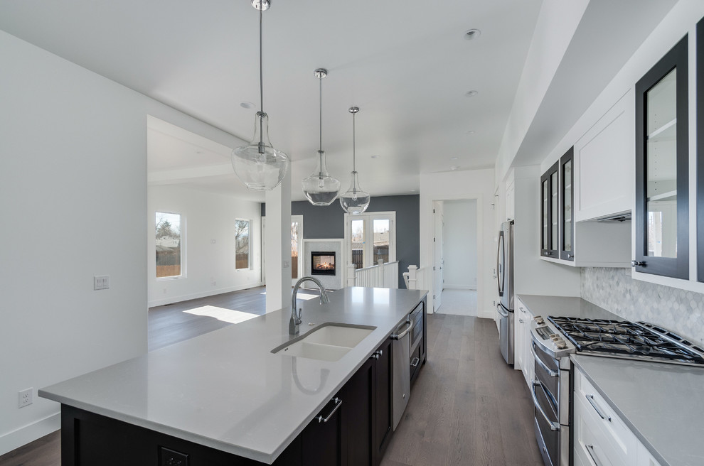 Example of a mid-sized transitional galley medium tone wood floor open concept kitchen design in Denver with an undermount sink, shaker cabinets, white cabinets, quartz countertops, gray backsplash, marble backsplash, stainless steel appliances, an island and gray countertops