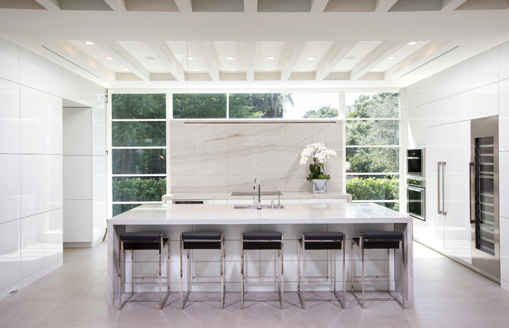 Bild på ett stort funkis kök, med släta luckor, vita skåp, bänkskiva i kvartsit, vitt stänkskydd, rostfria vitvaror, klinkergolv i porslin och en köksö