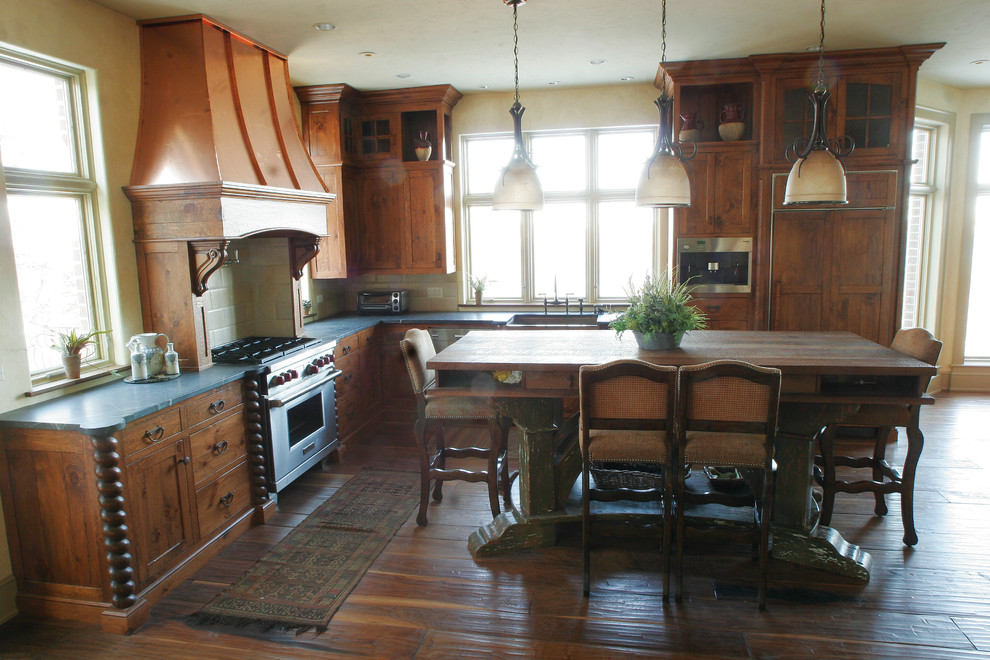 他の地域にあるラスティックスタイルのおしゃれなキッチン (エプロンフロントシンク、中間色木目調キャビネット、パネルと同色の調理設備、無垢フローリング) の写真