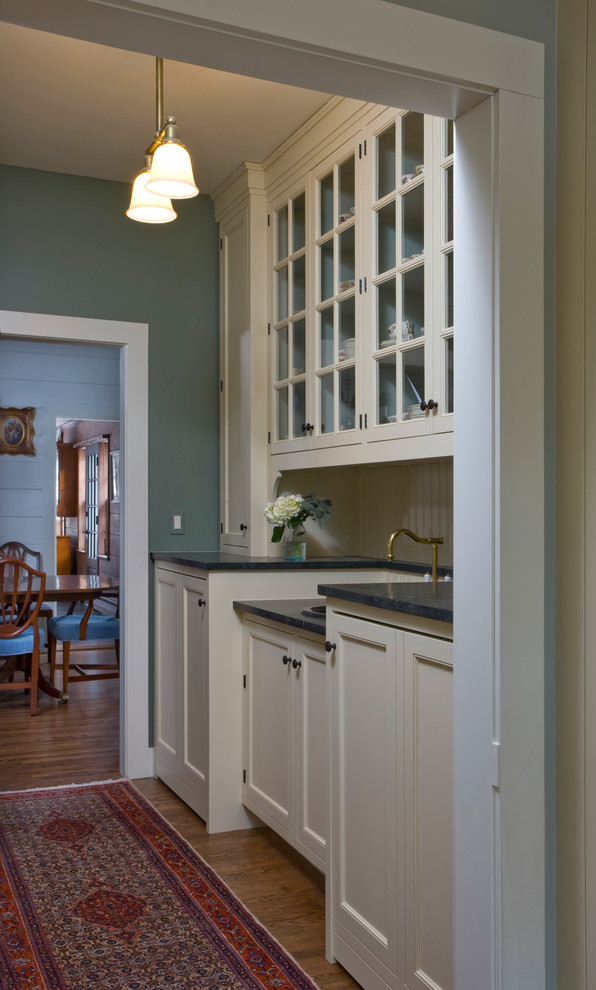 Example of a small classic galley medium tone wood floor enclosed kitchen design in Chicago with a farmhouse sink, beaded inset cabinets, white cabinets, soapstone countertops, colored appliances, no island and black countertops