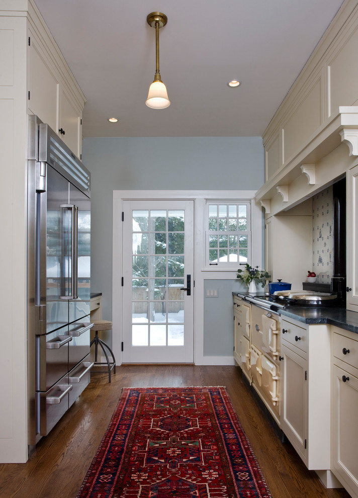 Small elegant galley medium tone wood floor enclosed kitchen photo in Chicago with a farmhouse sink, beaded inset cabinets, white cabinets, soapstone countertops, colored appliances, no island and black countertops