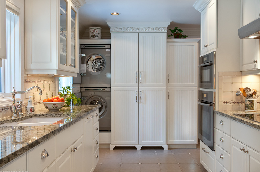 Cette photo montre une cuisine parallèle chic avec un évier encastré, un placard avec porte à panneau surélevé, des portes de placard blanches, un électroménager en acier inoxydable et machine à laver.