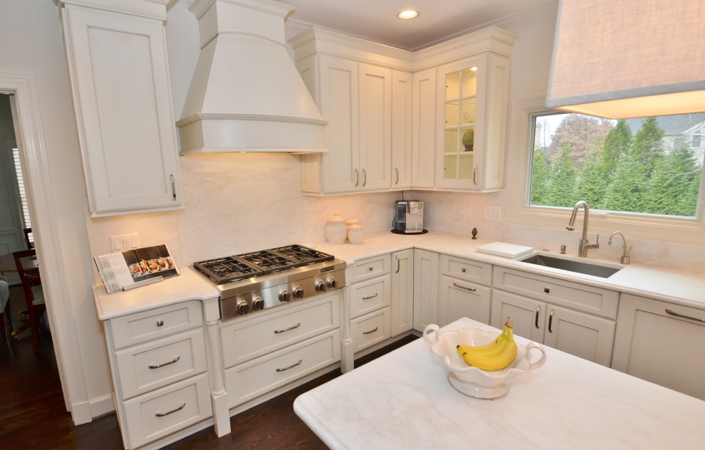 Example of a mid-sized classic u-shaped medium tone wood floor eat-in kitchen design in DC Metro with a drop-in sink, raised-panel cabinets, white cabinets, solid surface countertops, white backsplash, subway tile backsplash, stainless steel appliances and an island