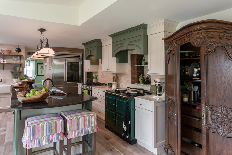 Design ideas for a large country galley kitchen/diner in Philadelphia with a belfast sink, recessed-panel cabinets, beige cabinets, engineered stone countertops, beige splashback, stone tiled splashback, coloured appliances, light hardwood flooring, an island and beige floors.