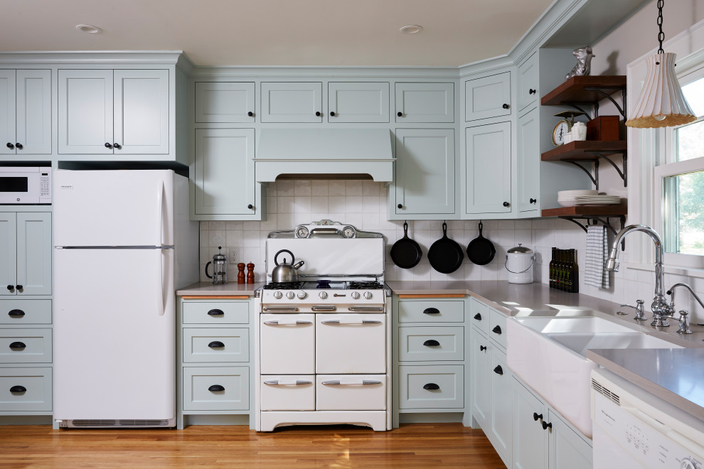 Inredning av ett lantligt grå grått l-kök, med en rustik diskho, skåp i shakerstil, blå skåp, vitt stänkskydd, vita vitvaror, mellanmörkt trägolv och brunt golv