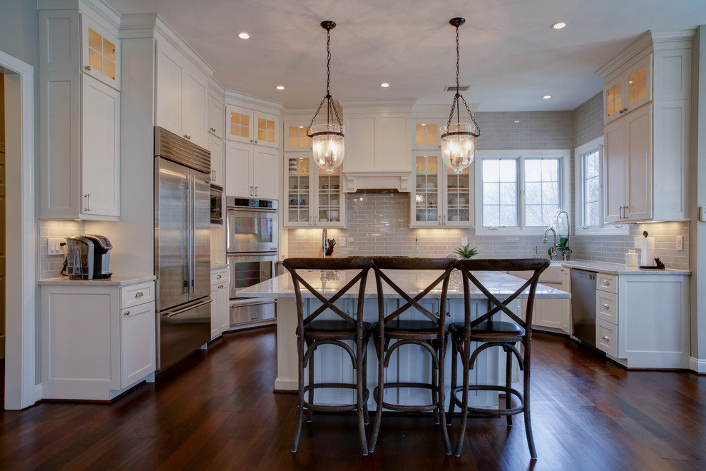 Inspiration for a large timeless u-shaped dark wood floor open concept kitchen remodel in DC Metro with a farmhouse sink, shaker cabinets, white cabinets, marble countertops, gray backsplash, subway tile backsplash, stainless steel appliances and an island