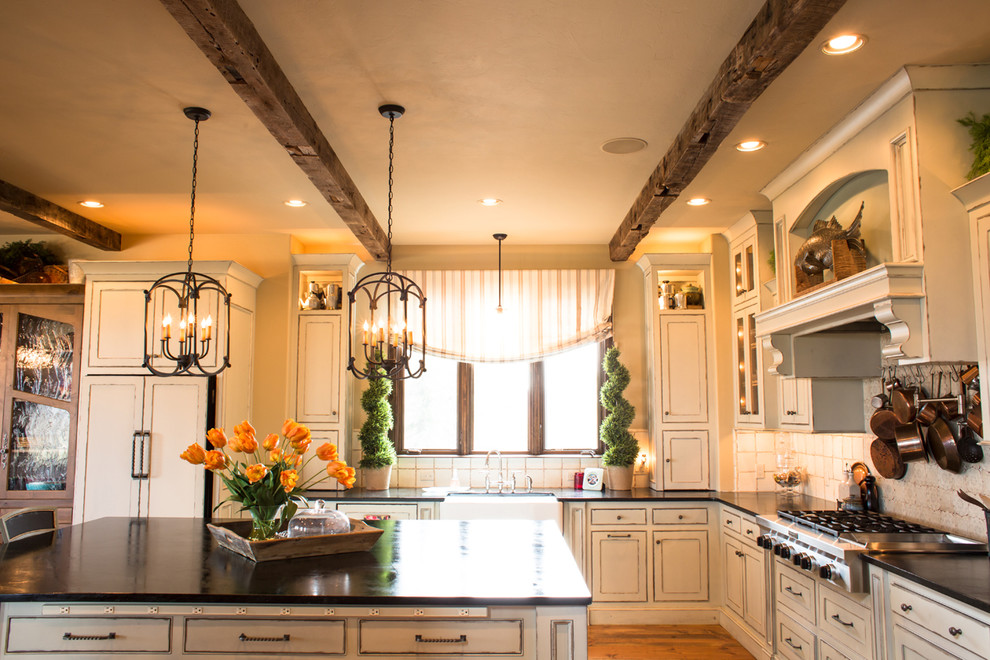 Bild på ett stort rustikt kök, med en rustik diskho, skåp i slitet trä, bänkskiva i täljsten, stänkskydd i terrakottakakel, rostfria vitvaror, mellanmörkt trägolv, en köksö, luckor med infälld panel och vitt stänkskydd