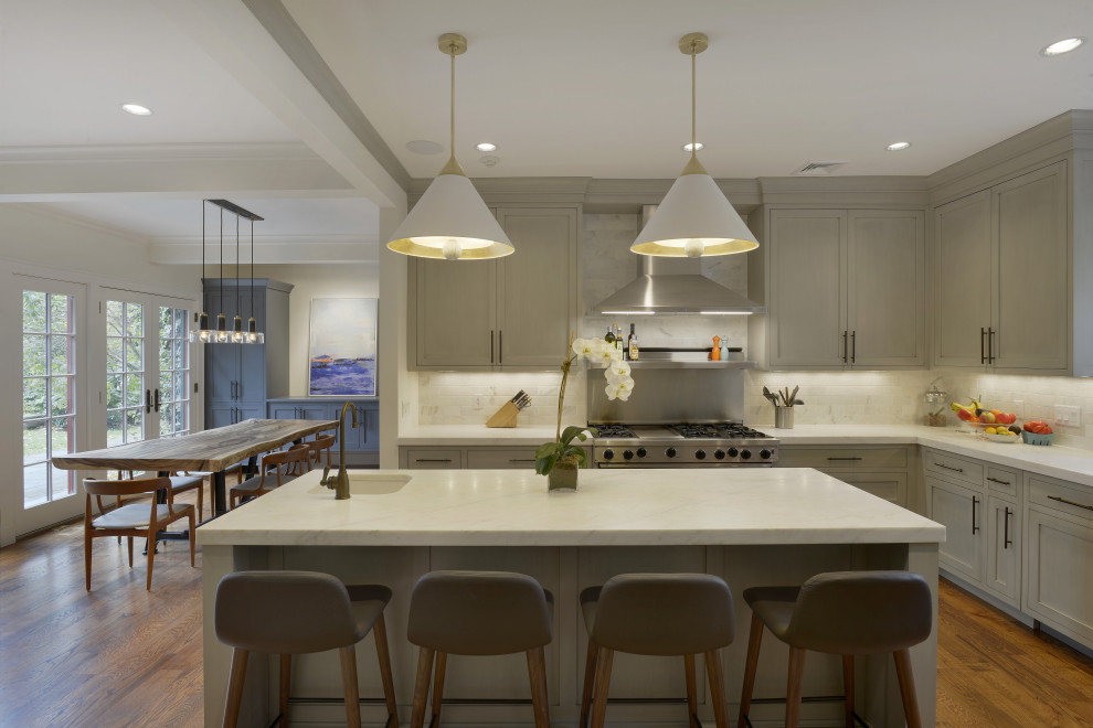 This is an example of an expansive classic l-shaped kitchen/diner in New York with grey cabinets, white splashback, metro tiled splashback, stainless steel appliances, medium hardwood flooring, an island, brown floors, white worktops and shaker cabinets.