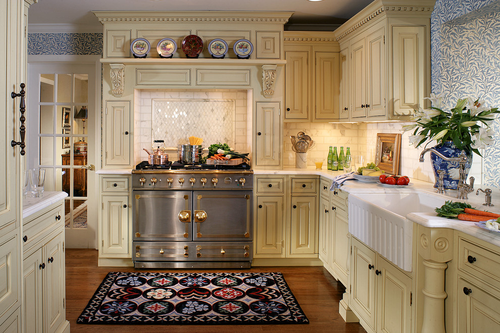 Kitchen - mid-sized traditional u-shaped medium tone wood floor kitchen idea in Newark with a farmhouse sink, beaded inset cabinets, yellow cabinets, marble countertops, white backsplash, stone tile backsplash and stainless steel appliances