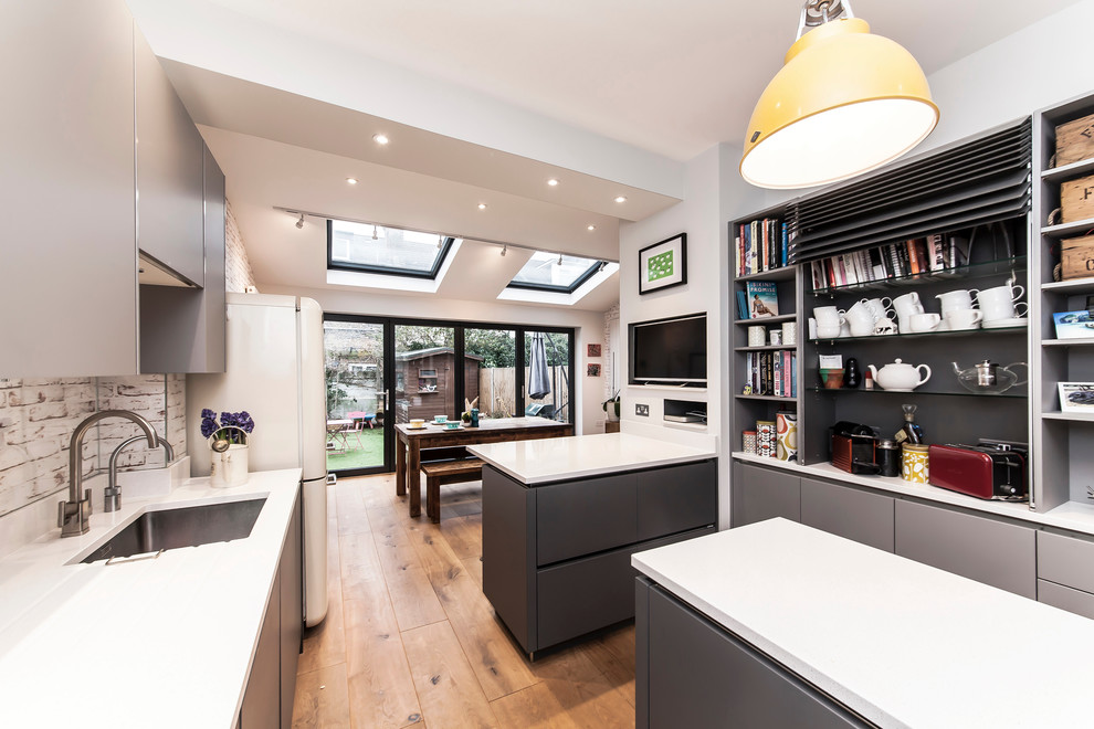 This is an example of a medium sized contemporary kitchen/diner in London with a submerged sink, flat-panel cabinets, grey cabinets, composite countertops, multi-coloured splashback, glass sheet splashback, stainless steel appliances, medium hardwood flooring and an island.
