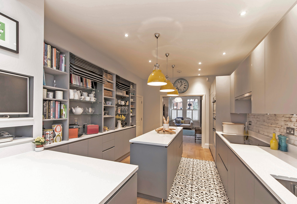 This is an example of a medium sized contemporary kitchen/diner in London with a submerged sink, flat-panel cabinets, grey cabinets, composite countertops, multi-coloured splashback, glass sheet splashback, stainless steel appliances, medium hardwood flooring and an island.