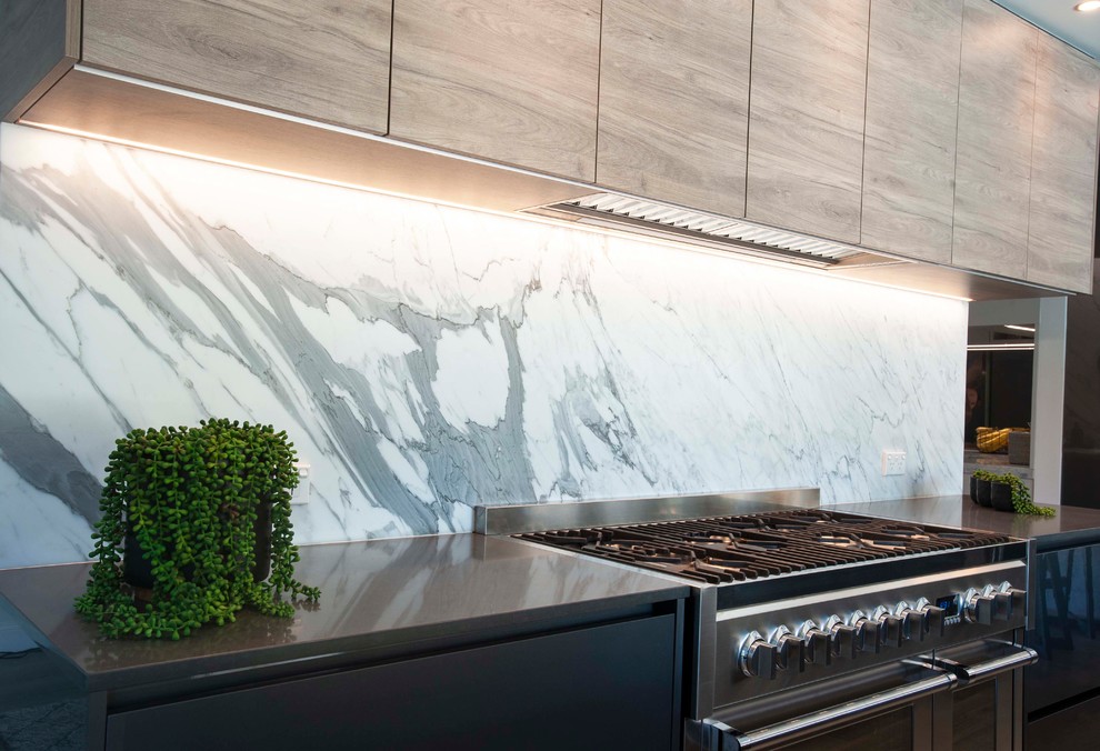 Idée de décoration pour une grande cuisine ouverte parallèle design avec un évier posé, plan de travail en marbre, une crédence en dalle de pierre, un électroménager noir et îlot.