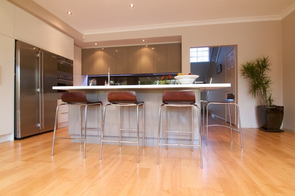 Mittelgroße Moderne Wohnküche in L-Form mit Triple-Waschtisch, weißen Schränken, Glasrückwand, Küchengeräten aus Edelstahl, Kücheninsel, flächenbündigen Schrankfronten, Mineralwerkstoff-Arbeitsplatte, Küchenrückwand in Schwarz und hellem Holzboden in Sydney