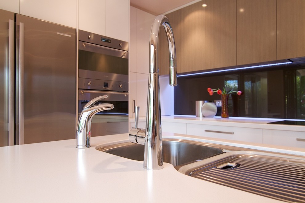 Immagine di una cucina moderna di medie dimensioni con lavello a tripla vasca, ante bianche, paraspruzzi con lastra di vetro, elettrodomestici in acciaio inossidabile, ante lisce, top in superficie solida, paraspruzzi nero e parquet chiaro