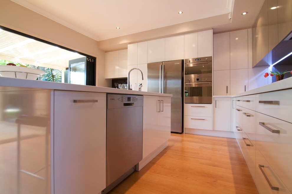 Bild på ett mellanstort funkis kök, med en trippel diskho, vita skåp, glaspanel som stänkskydd, rostfria vitvaror, en köksö, släta luckor, bänkskiva i koppar, svart stänkskydd och ljust trägolv