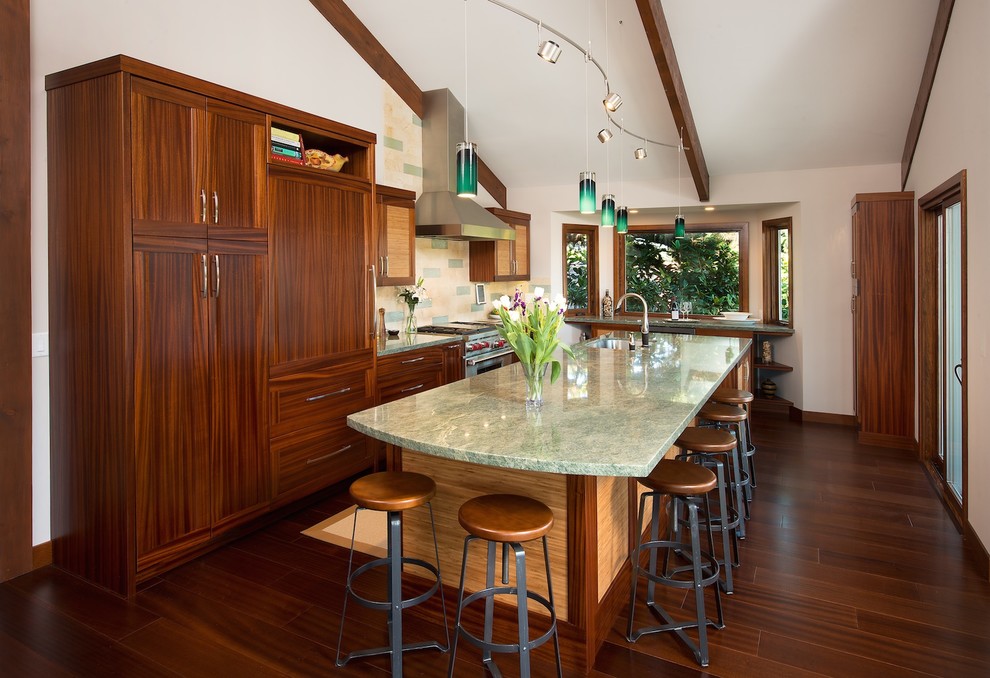 Cette image montre une cuisine américaine encastrable traditionnelle en L et bois brun de taille moyenne avec un évier encastré, un placard à porte plane, un plan de travail en granite, une crédence beige, une crédence en carrelage de pierre, parquet foncé, îlot et un sol marron.