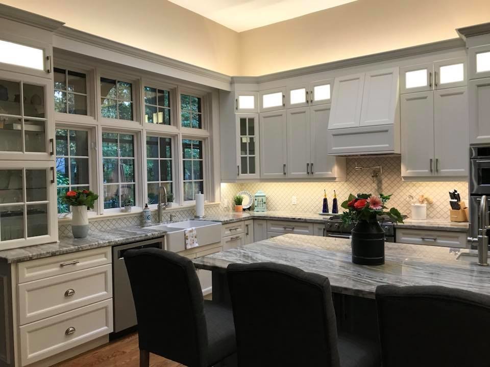 Large transitional l-shaped medium tone wood floor kitchen pantry photo in Toronto with a farmhouse sink, recessed-panel cabinets, white cabinets, granite countertops, white backsplash, porcelain backsplash, stainless steel appliances, an island and blue countertops