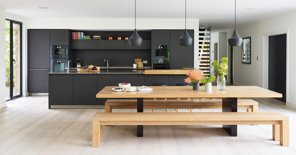 Diseño de cocina contemporánea con armarios con paneles lisos, puertas de armario negras, electrodomésticos negros, suelo de madera clara, una isla y suelo beige