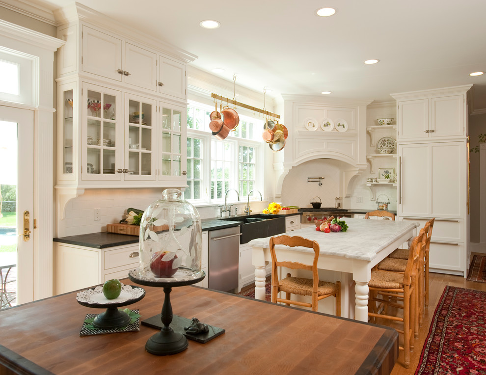 Klassische Küche in L-Form mit Landhausspüle, Kassettenfronten, weißen Schränken, Küchenrückwand in Weiß, Rückwand aus Metrofliesen und Elektrogeräten mit Frontblende in Boston