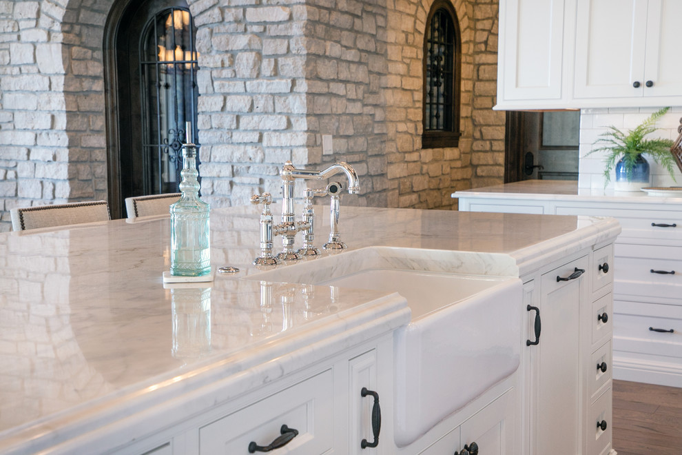Example of a large transitional u-shaped medium tone wood floor and brown floor kitchen design in Milwaukee with a farmhouse sink, recessed-panel cabinets, white cabinets, quartzite countertops, two islands, white backsplash, subway tile backsplash, paneled appliances and white countertops