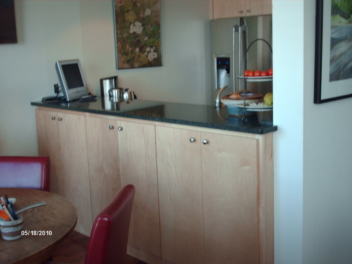 Cette photo montre une petite cuisine ouverte parallèle moderne en bois clair avec un évier encastré, un placard à porte plane, un plan de travail en quartz modifié, une crédence rouge, une crédence en carreau de verre, un électroménager en acier inoxydable et un sol en liège.