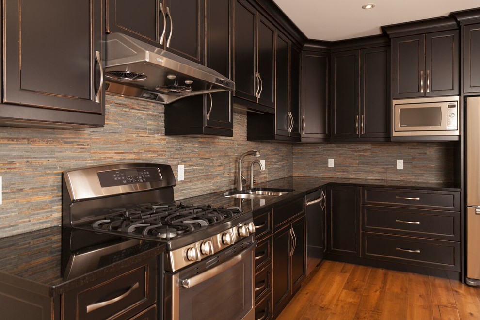 Photo of a medium sized traditional l-shaped open plan kitchen in Toronto with a double-bowl sink, recessed-panel cabinets, dark wood cabinets, composite countertops, grey splashback, stone tiled splashback, stainless steel appliances, medium hardwood flooring and no island.